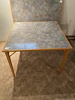 Full view of the square laminate top folding table with wooden frame on carpeted floor.