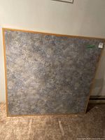 Closed view of table top leaning against wall showing textured laminate top with a light wood frame.