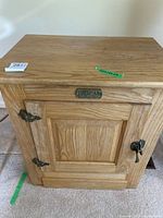 Front view of small oak cupboard showing door, metal hinges, latch, and raised panel design