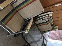 Set of one square patio table with clear textured glass on metal frame and four stacked folding chairs with striped fabric seats, visible wear and stains on chairs.