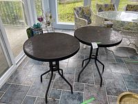 Two round metal tables shown side-by-side on tiled floor, black legs with round brown tops, minor wear visible