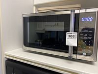 Silver and black countertop microwave sitting on a white surface, showing the front door with control panel and LED display.