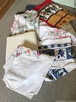 Lot of multiple small tablecloths in different designs and colors spread on carpet.