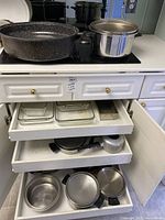 Cookware including large black speckled roasting pan, stainless steel pot with lid, metal pans in open drawers
