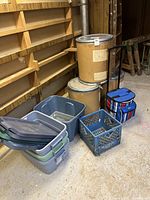 Wide view showing all storage bins stacked, cardboard drums seated behind, milk crate, and wheeled cooler.