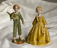 Photo showing both Royal Worcester bone china porcelain figurines together on a neutral fabric background: The Parakeet and Grandmother's Dress.