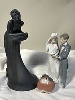 Front view of three porcelain figurines: black Royal Doulton female figure, small brown bird, and Lladro bride and groom couple.