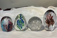 Front view showing four different vintage blown art glass paperweights with varied colors and internal designs.