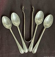 Five Birks sterling silver pieces including four espresso spoons and sugar cube tongs laid out on dark cloth.