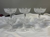Front view of all six cut crystal glasses arranged in two rows on a white cloth, showing intricate cut pattern and clear crystal.