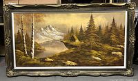 Full view of large framed oil painting showing the landscape scene with mountains, lake, pine trees, and cabin.