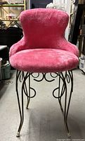 Front view of a hot pink fuzzy vanity chair with brass swirl legs in a warehouse setting.