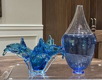 Photo showing both vase and bowl side by side on a wooden surface, clear lighting shows glass colors and shapes.