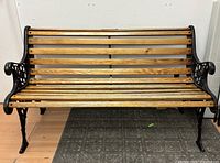 Front view of garden bench showing full seating area with wood slats and black cast iron frame with decorative arms and legs.