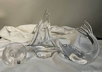 Three crystal paperweights: clear Daum sailboat, Mats Jonasson bear, Ronneby dolphin on white fabric background.