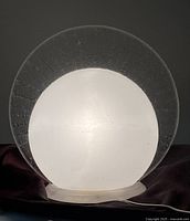 Front view of the acrylic scalloped table lamp illuminated, showing frosted globe in front of clear scalloped disc.