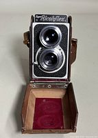 Front view of Super Ricohflex camera with open leather case showing interior and twin lenses.