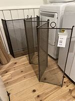 Larger and smaller antique folding metal mesh fire screens viewed from an angle, showing folding panels and loop handles