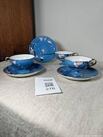Three Noritake cups and saucers with blue background and handpainted plum blossoms, showing overall lot contents.