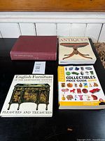 Four antique reference books displayed on a black surface against a white wood-panel background.