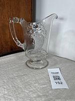 Antique clear glass pitcher with embossed cornucopia and cherries design shown from front side