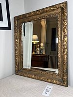 Front view of the rectangular antique beveled mirror with ornate gilt frame, showing its detailed baroque floral and scroll carvings.