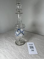 Front view of the clear glass decanter showing blue and white enamel floral chevron design