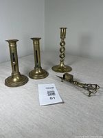 Overall view of two brass candlesticks, one spiral stem candlestick, and brass snuffer scissors on table