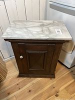 Full front view of antique wooden cabinet with white marble slab top, showing door with round white knob and wood paneling.