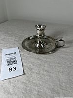 Antique Christofle silver plate chamber stick with integrated handle on neutral fabric background, showing overall condition and wear.