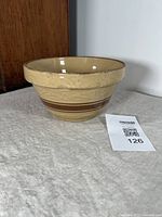Side profile of beige glazed stoneware mixing bowl with brown decorative stripe, showing slight glaze crazing and light wear.