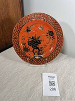 Front view of red decorative plate with black and gold birds and flowers, lattice rim