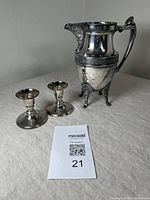 Full view of the silver plate Reed & Barton Eastlake style footed pitcher and two matching vintage candlesticks on table with lot card.