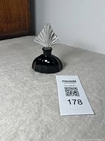 Full view of assembled black glass perfume bottle with clear glass fan-style stopper on top.