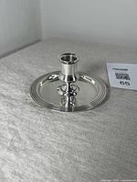 Front angled view of silver plate candlestick holder showing reflective finish and concentric circle design on base.