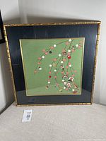 Framed silk scarf with green fabric background and black fabric matting in gold-tone bamboo style frame.