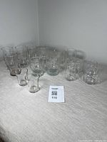 Wide view showing all 15 vintage clear glassware pieces on a light surface in neutral background.