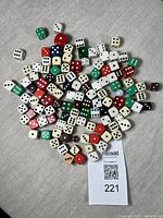 Photo showing a large assortment of vintage dice in multiple colors and sizes scattered on a grey surface with a MaxSold lot tag visible.
