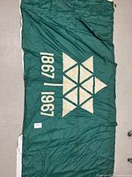 Full view of the green flag laid flat, showing cotton-patch maple leaf logo and dates