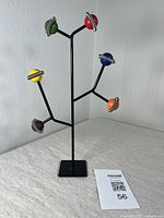 Full front view of the black metal jewelry stand with 6 colored spheres adorned with metal coil rings, standing on a square base.