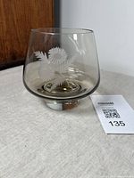 Smoked glass vase showing acid etched floral motif, beveled rim, and rounded shape on flat surface