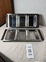 Front view of two vintage stainless steel divided trays with rosewood handles placed on a cloth surface, showing their rectangular shape and three compartments each.