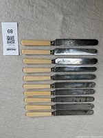 Set of 10 Victorian dinner knives with cream composite handles and steel blades lined up on a flat surface.