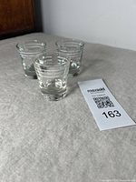 Three mid-century shot glasses on table showing front side with embossed branding and measurement markings