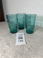 Three turquoise glass highball tumblers standing upright on a flat surface with a MaxSold auction lot card in front.