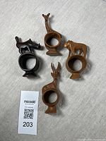 Four hardwood napkin rings shaped as African animals: giraffe, lion, gazelle, and rhinoceros, arranged upright on a light surface with a MaxSold tag.