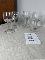 Four vintage blown glass crystal coupes or small wine glasses viewed from the side on a table with a white cloth.