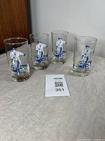 Four vintage Dominion drinking glasses with blue and white curling player graphics arranged on table showing front views of the graphics.