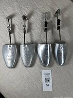 Four vintage metal shoe stretchers arranged on fabric background showing front toe portion including retailer markings.