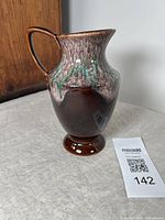 Full side view of the ceramic drip glaze pitcher showing the detailed gradient from brown to green glaze, label attached and the round base on a flat surface.